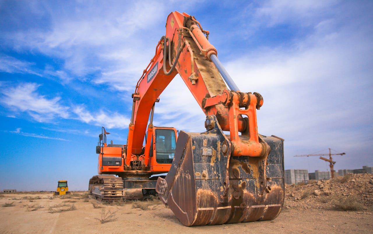 our-story A large orange excavator working on a construction site under a blue sky.